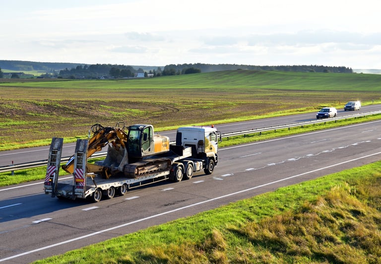 Flatbed truck transporting heavy excavator machinery on highway